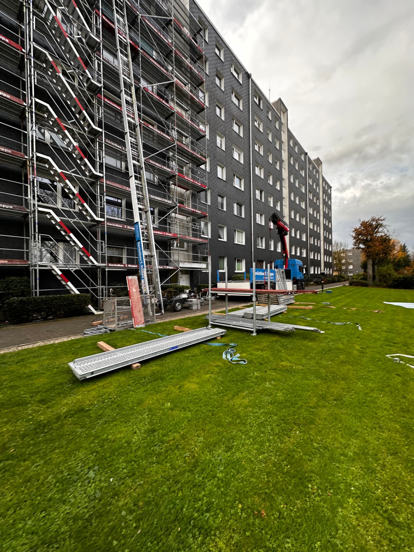 Mobiler Bauaufzug an einem voll eingegrüsteten Wohnhochhaus von Gerüstbau Stoppa, Stoppa-Lkw mit Ladekran davor