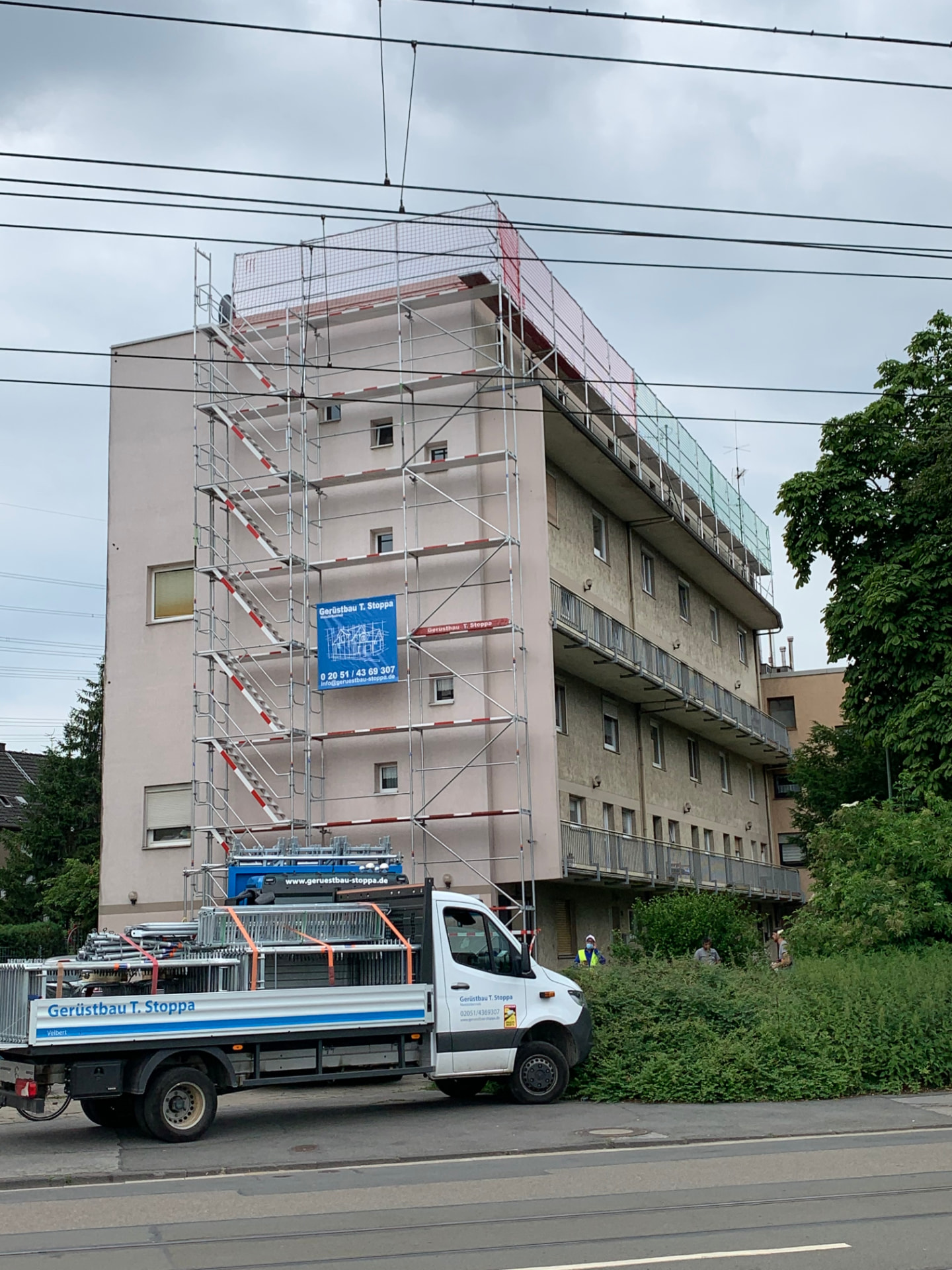 Echtes Stoppa-Projekt: Gerüst mit Dachfangsicherung an einem Mehrfamilienhaus, davor ein Gerüstbau-Stoppa-Lkw