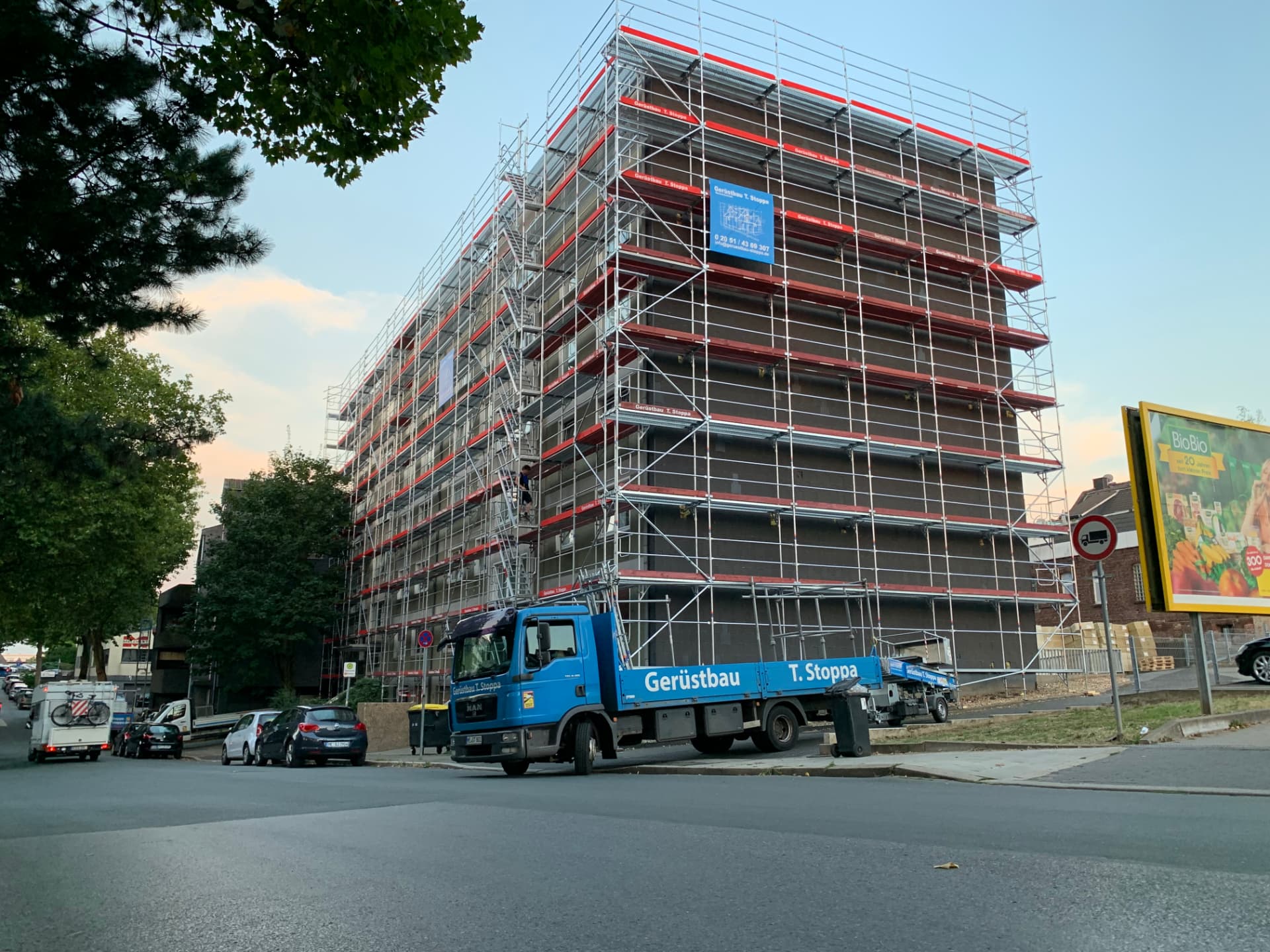 Echtes Stoppa-Projekt: mehrgeschossiges Gebäude mit vollständig montiertem Fassadengerüst, davor ein blauer Gerüstbau-Stoppa-Lkw
